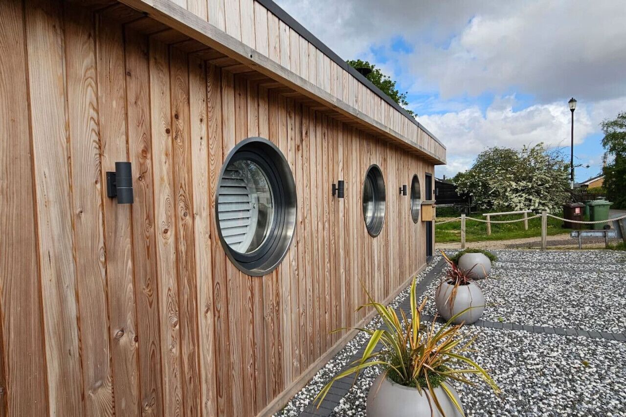 Un bâtiment en bois doté de fenêtres rondes et d’un chemin de gravier bordé de plantes en pot.