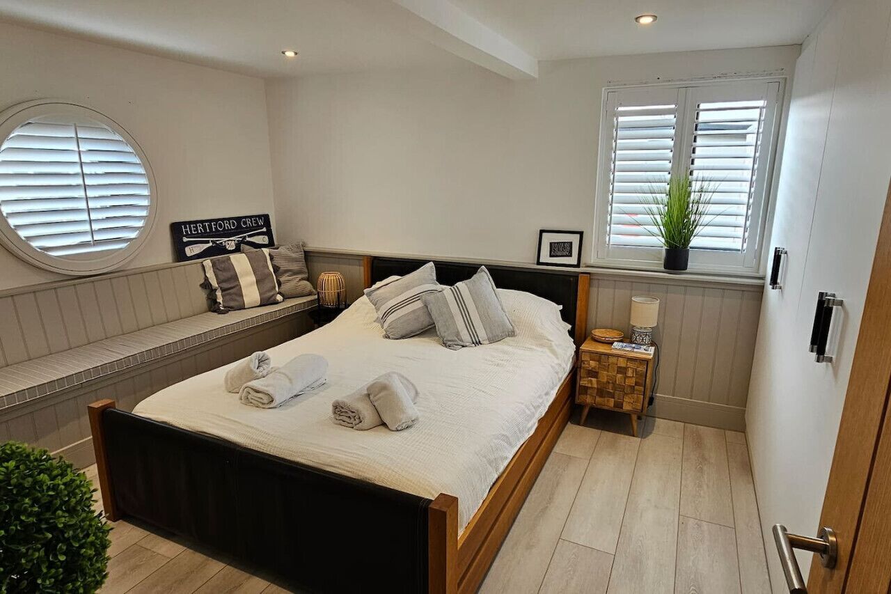 Un lit bien fait, avec des oreillers et des serviettes, une table de chevet avec une lampe, une fenêtre avec des stores et un panneau accroché au mur.