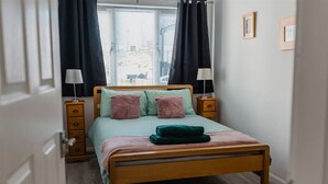 Un dormitorio con una cama de madera, dos mesitas de noche con lámparas, una ventana con persianas y una puerta.