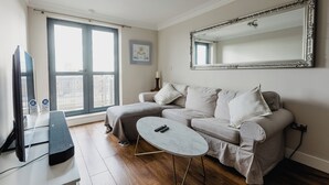 En moderne stue med sofa, sofabord, fjernsyn og et stort spejl.