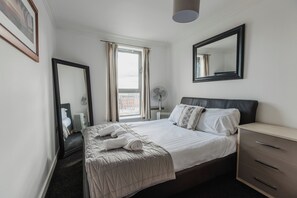 Ett hotellrum med en säng, en byrå, en spegel och ett fönster med gardiner.
