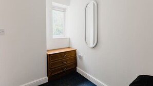 A small, clean room with a wooden dresser, a white wall, and a window. - Withernsea Studio Apt + Sofa bed (Withernsea)