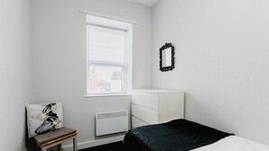 A small, neatly arranged bedroom with a single bed, a chair, a dresser, and a window with blinds. - Withernsea Studio Apt + Sofa bed (Withernsea)