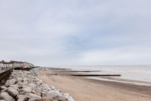 A beach with a rocky shoreline, a pier extending into the sea, and a row of buildings along the coast. - Withernsea Studio Apt + Sofa bed (Withernsea)