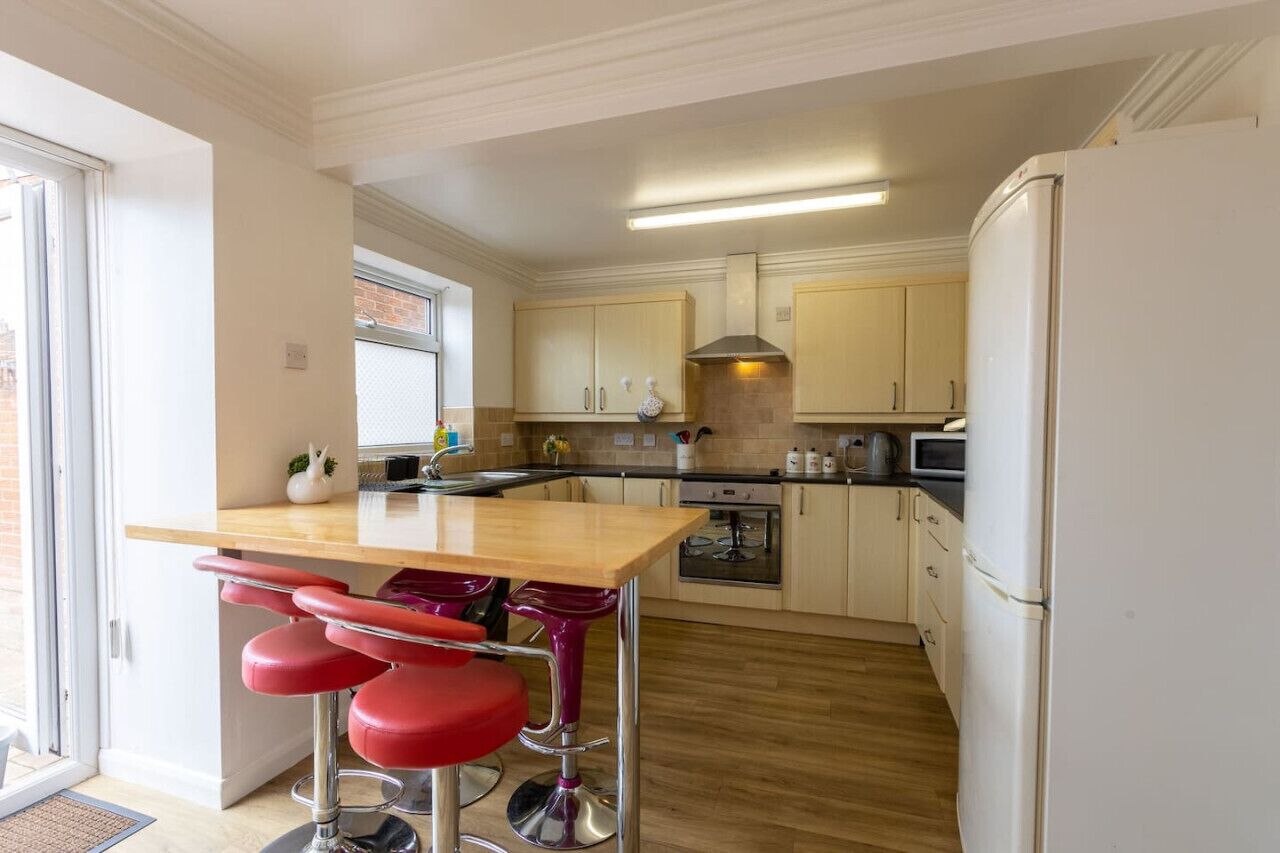 A modern kitchen with a wooden island, red bar stools, and a white refrigerator.