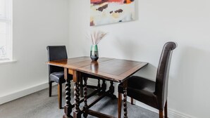 A dining table with four chairs, a vase with dried plants, and a colorful abstract painting on the wall. - Hullidays》Withernsea Duplex Apt (Withernsea)
