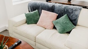 A white sofa with three cushions in green and pink, a remote control on a wooden coffee table, and a dining table with chairs in the background. - Hullidays》Withernsea Duplex Apt (Withernsea)