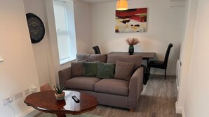 A living room with a brown sofa, a round wooden coffee table, a small potted plant, and a painting on the wall. - Hullidays》Withernsea Duplex Apt (Withernsea)