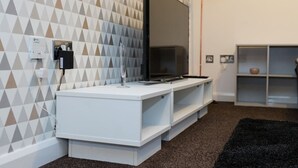 Ein modernes Wohnzimmer mit einem Flachbildfernseher auf einer weißen Unterhaltungsanlage, geometrischem Wandpapier und einem schwarzen Teppich.