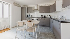 Eine moderne Küche mit grauen Schränken, einer weißen Arbeitsplatte und einem Essbereich mit Holztisch und Stühlen.