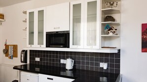 Una cocina moderna con armarios blancos, salpicadero de azulejos negros, microondas y cafetera.