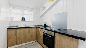 A kitchen with wooden cabinets, a black countertop, and a window with blinds. - Withernsea Coastal Getaway Apt (Withernsea)