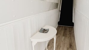 A narrow hallway with a white wall, a small white table with a magazine, and a black door at the end. - Withernsea Coastal Getaway Apt (Withernsea)