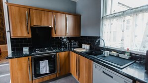 A modern kitchen with wooden cabinets, black countertops, and stainless steel appliances.