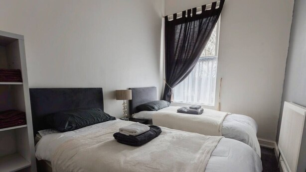 A room with two beds, a wardrobe, a window with curtains, and a radiator.