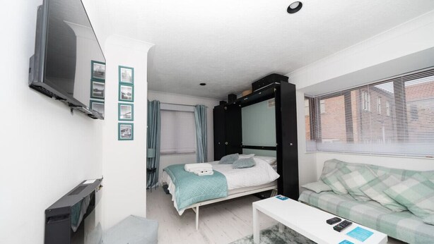 Une pièce de taille modeste comprenant un lit, un canapé, un téléviseur fixé au mur et une petite table.