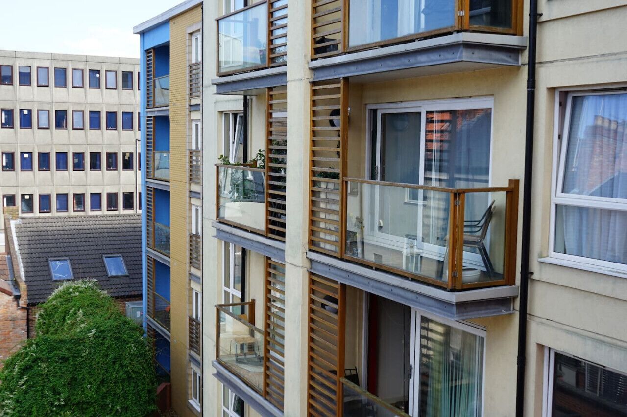 Un immeuble résidentiel à plusieurs étages, doté de balcons, de grandes fenêtres et d’un espace jardin visible.