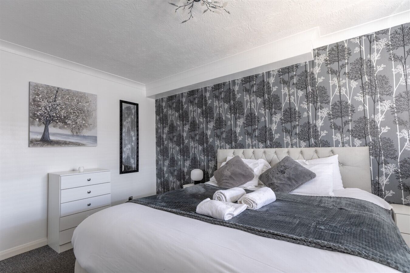 Une chambre à coucher comprenant un lit, une table de chevet, une commode et une lampe fixée au mur.
