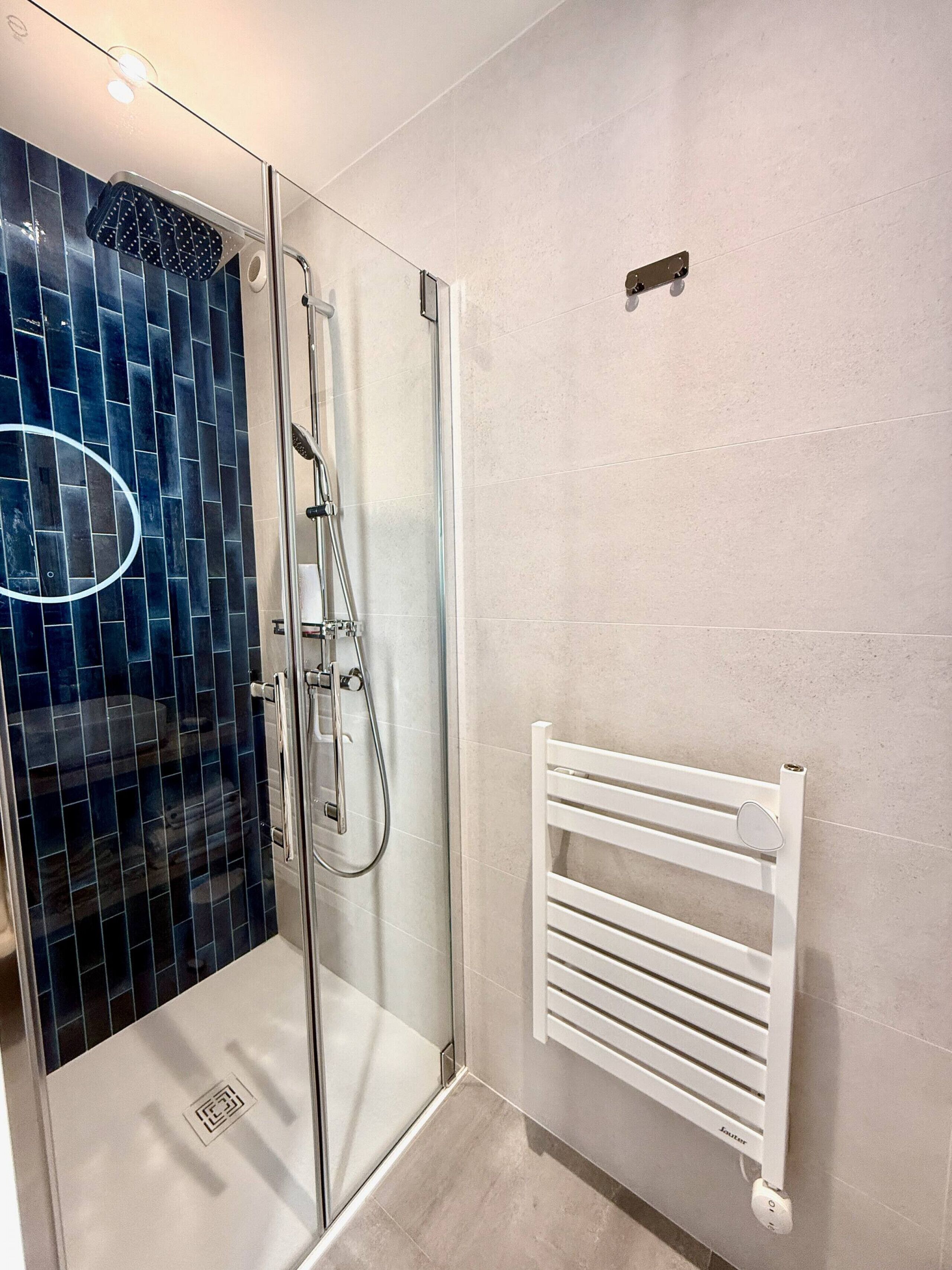 A shower with a glass door, a white towel rack, and a tiled wall.
