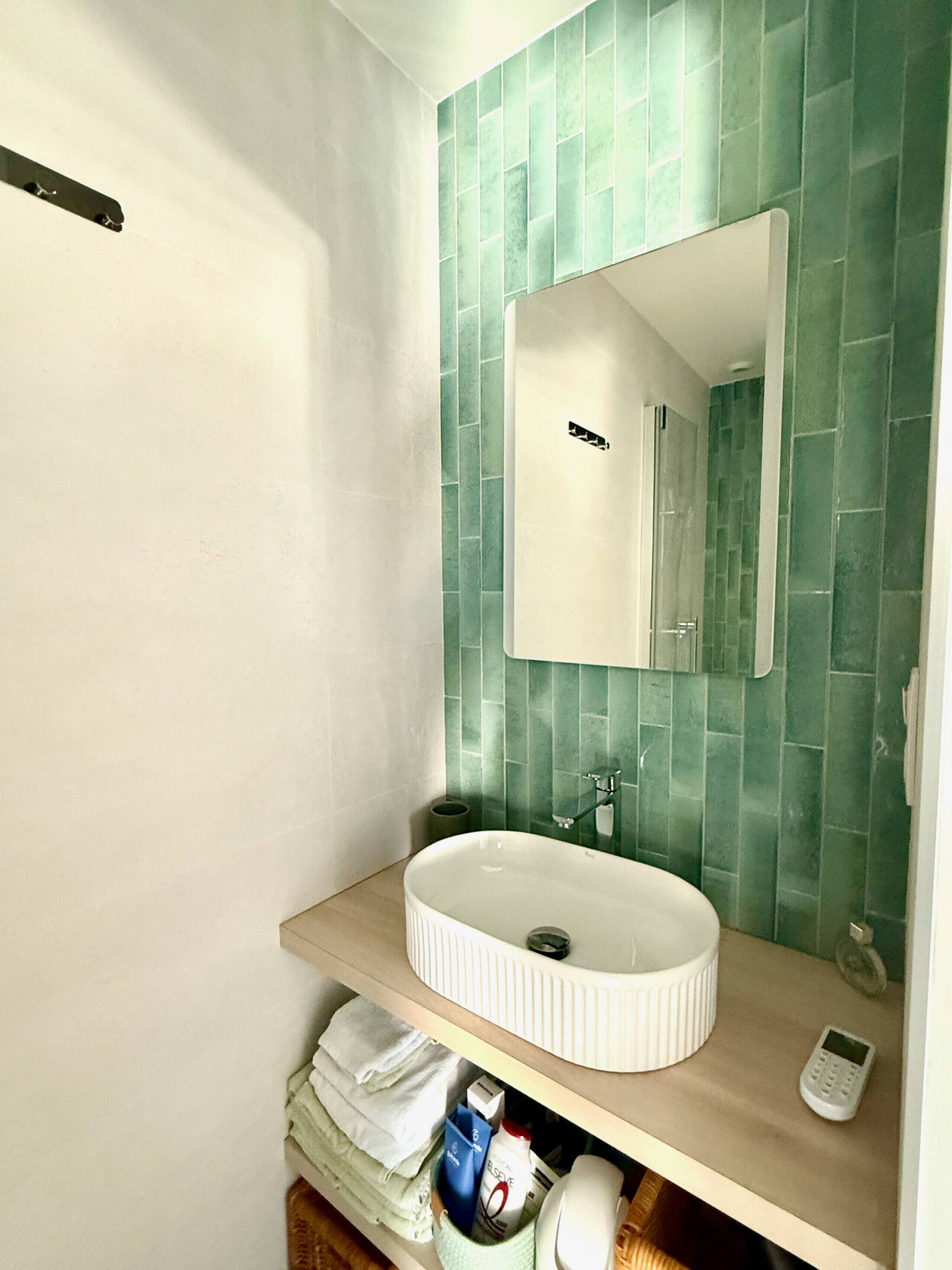 A bathroom with a white sink, green tiled walls, a mirror, and a towel rack.