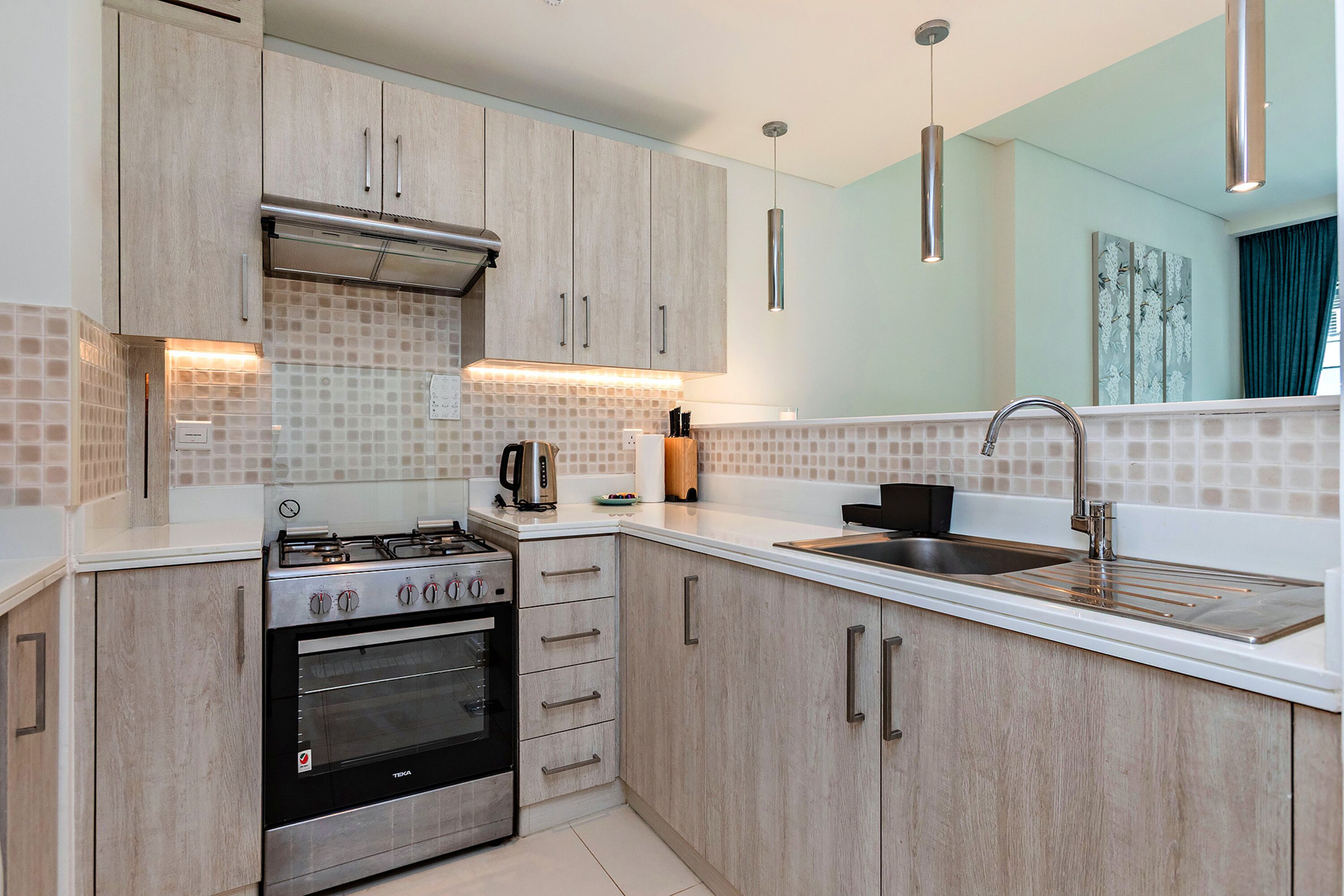 A modern kitchen with light wood cabinets, a stainless steel stove, and a double sink.