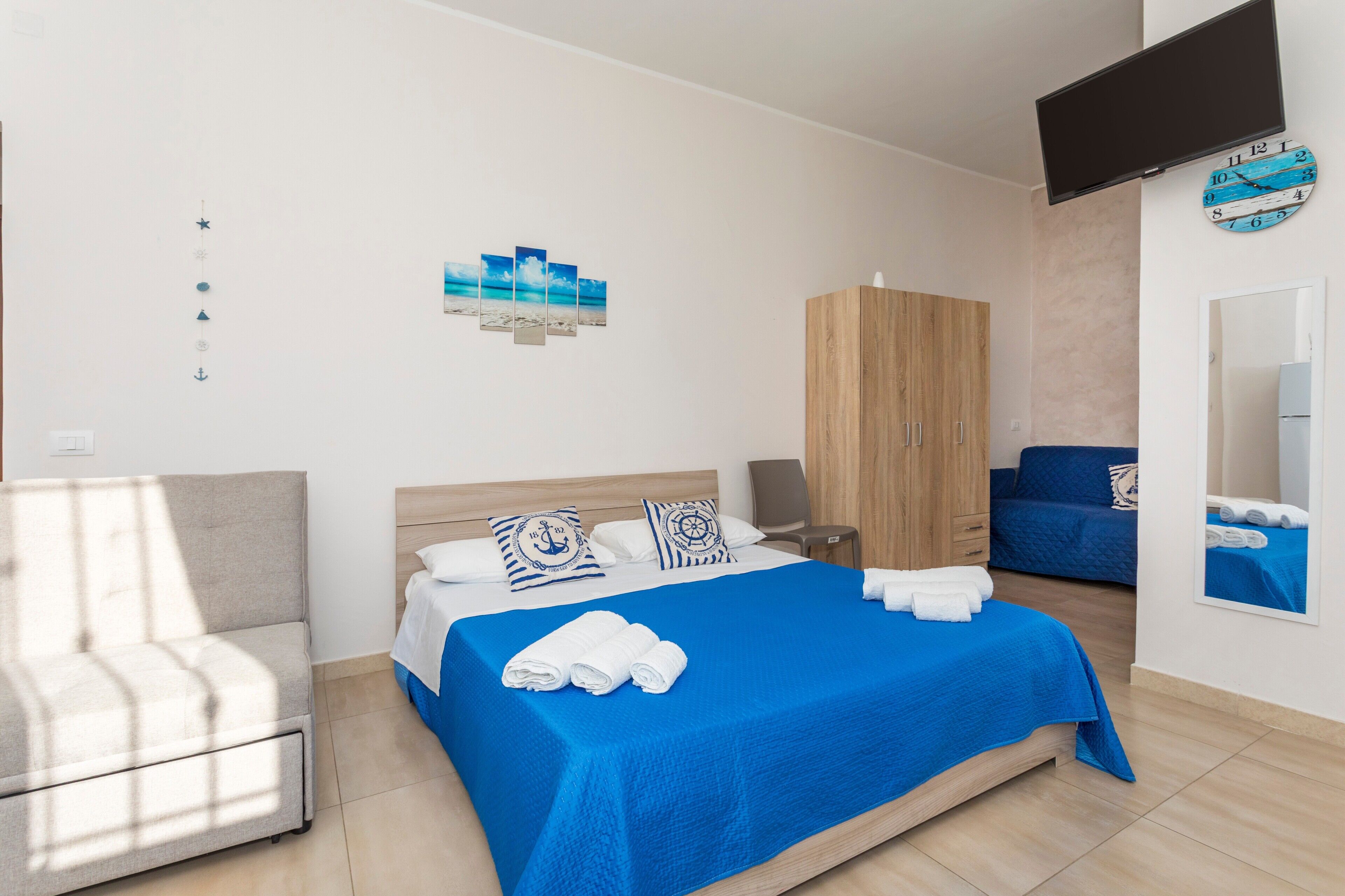 Un dormitorio con cama, armario, televisor y un pequeño rincón de descanso.