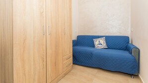 Een kamer met een houten garderobe, een blauwe gewatteerde bank en een kussen met een patroon.