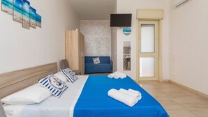 Een slaapkamer met een bed, een blauwe deken, een televisie, een kledingkast en een deur.