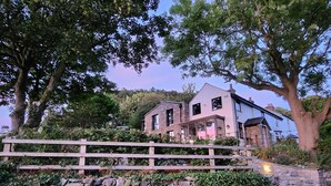 A two-story stone house with a stone wall and wooden fence in front. - Windyridge (Rhyl)