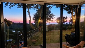 A room with a large sliding glass door leading to a garden. Inside, there is a table with a book and a chair. - Windyridge (Rhyl)