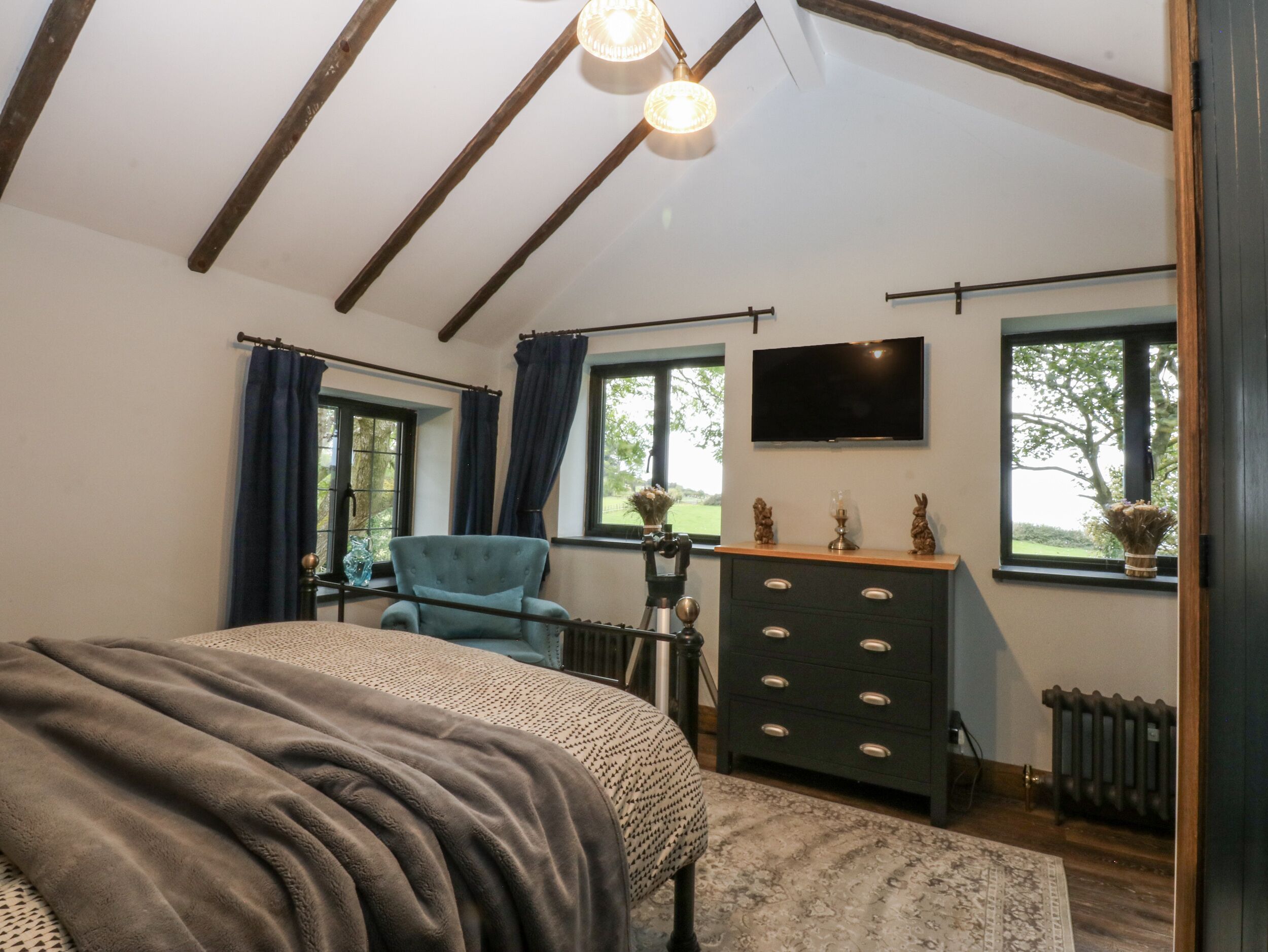 A bedroom with a bed, a dresser, a chair, a television, and a window with a view of greenery.