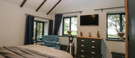A bedroom with a bed, a dresser, a chair, a television, and a window with a view of greenery.