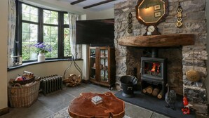 A cozy living room with a stone fireplace, a large window with curtains, a wooden table, and a television mounted on the wall. - Windyridge (Rhyl)