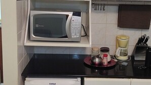 Una cucina compatta con forno a microonde, macchina del caffè e piccolo frigorifero.