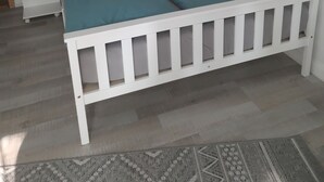 Ein weißes Bett mit türkisfarbenem Bettzeug in einem Zimmer mit einem weißen Nachttisch, einer Lampe und einem gemusterten Teppich.