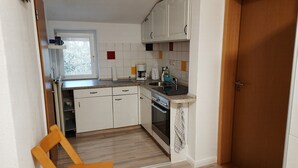 Eine kleine Küche mit weißen Schränken, einem eingebauten Backofen und einem Fenster.