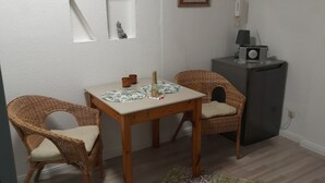 Ein kleiner Essbereich mit einem Tisch, zwei Korbstühlen, einem gemusterten Teppich und einem Kühlschrank.
