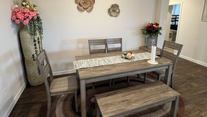 A dining area with a wooden table, chairs, and a bench. There are decorative wall pieces and a vase with flowers.