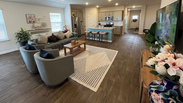 A modern living room with a grey sofa, a coffee table, and a kitchen area in the background.