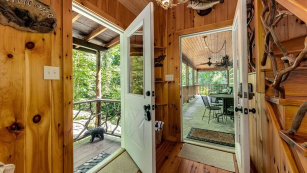 A wooden cabin with a welcoming sign, a covered porch, and a dining area with outdoor seating.
