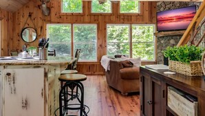 A rustic cabin interior with a kitchen area, dining space, and a cozy living area with a fireplace.