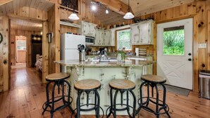 A rustic cabin kitchen with wooden walls, a central island with stools, a refrigerator, a microwave, and a 'No Smoking' sign.