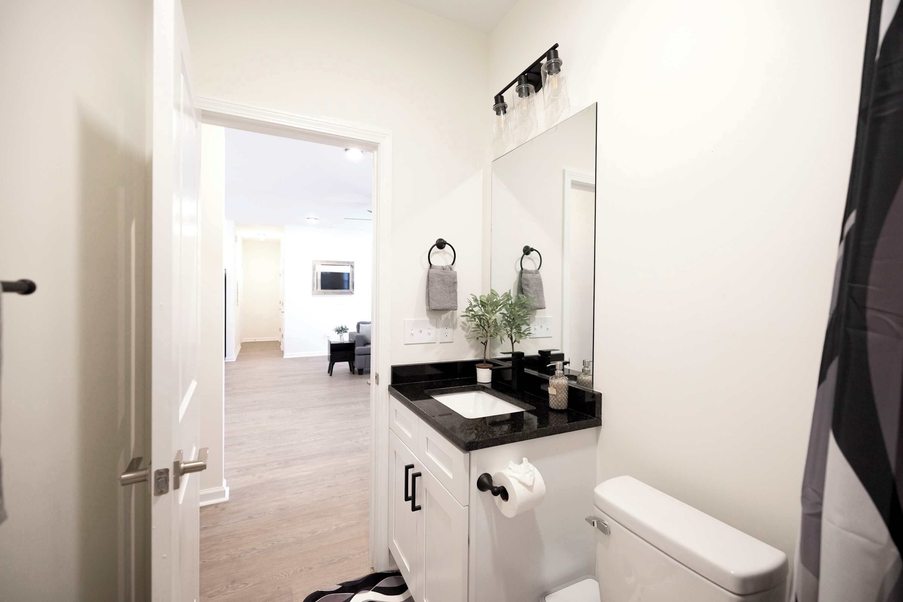 Un baño moderno con inodoro blanco, encimera negra, espejo grande y un perchero para toallas.