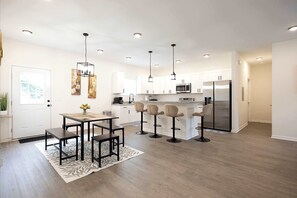 Una cocina moderna con armarios blancos, una isla central, taburetes de bar e iluminación colgante.