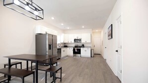 A modern kitchen with white cabinets, stainless steel appliances, and a dining area with a dark wooden table and benches. - 4 Min to Downtown | 10 to Elon | Car Rental Avail. (Burlington)