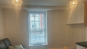 A living room with a black leather sofa, a wooden dining table with placemats, and a window with blinds. - The Courtyard Retreat (Sligo)