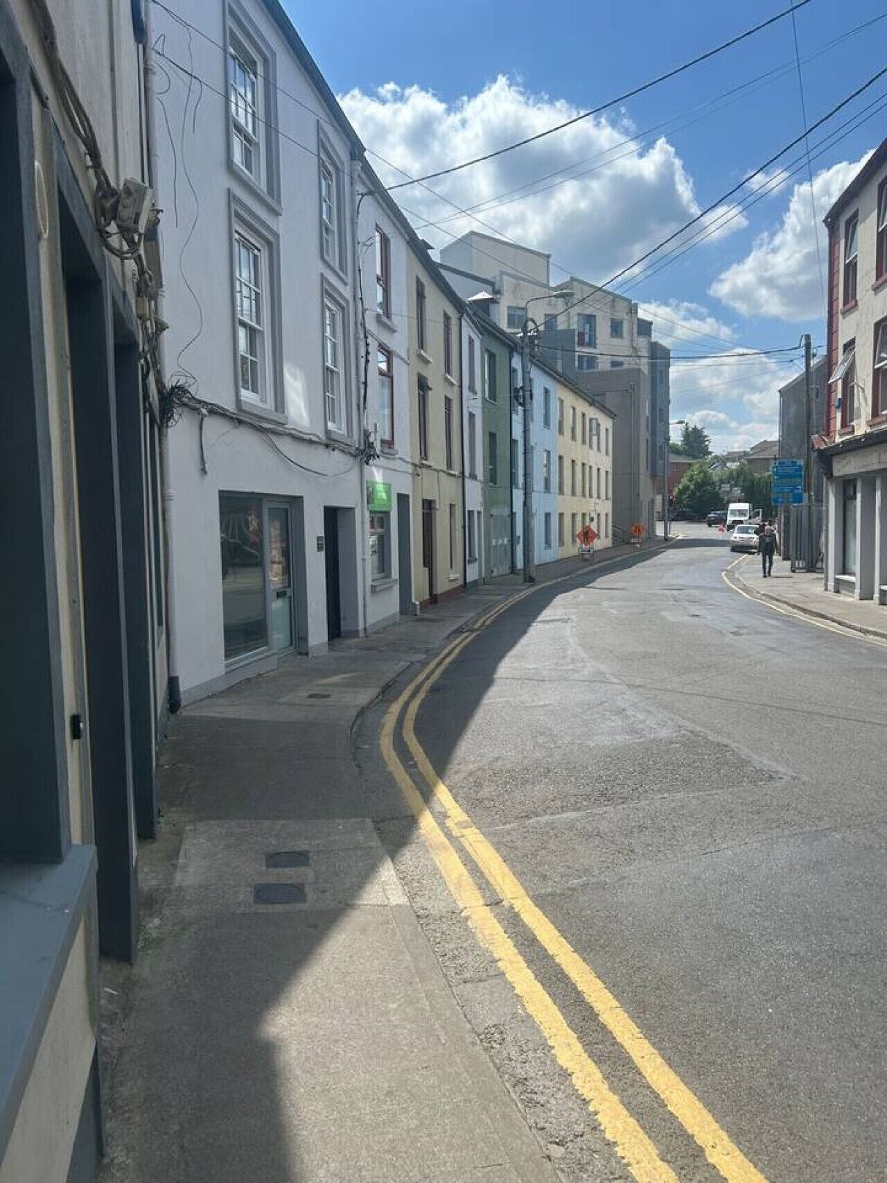 Une rue bordée de bâtiments des deux côtés, avec un trottoir et une chaussée délimitée par deux lignes jaunes continues.