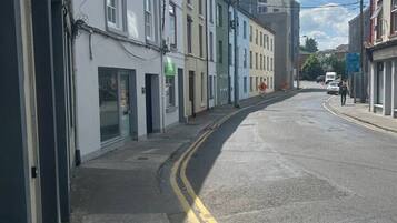 Une rue bordée de bâtiments des deux côtés, avec un trottoir et une chaussée délimitée par deux lignes jaunes continues.