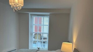 A bedroom with two beds, a chandelier, a window with blinds, and a bedside lamp. - The Courtyard Retreat (Sligo)