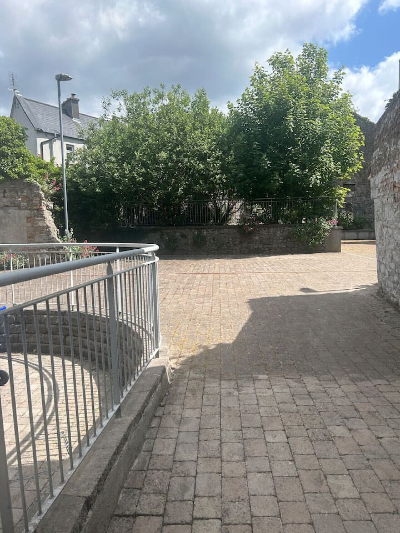 A paved courtyard with a metal railing, stone walls, and trees.